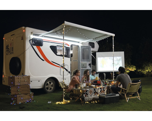 Vonkajšia scéna s obytným vozidlom, markízou, svetelnými reťazami a ľuďmi sledujúcimi plátno