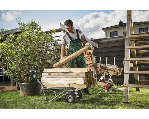 Muž nakladá do transportného vozíka palivové drevo na záhrade.