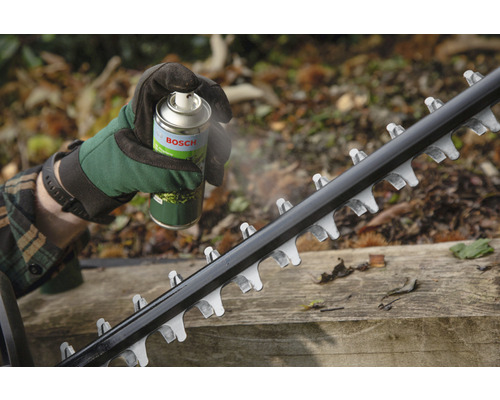 Osoba strieka čepeľ nožníc na živý plot údržbovým sprejom Bosch.