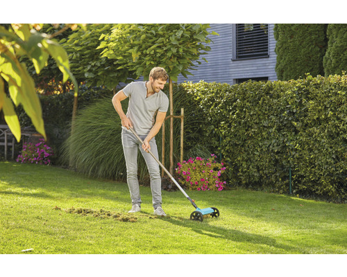 Muž používa zametač trávnika v záhrade na odstránenie trávnatého odpadu.