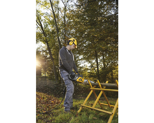 Muž pília elektrickou pílou klát dreva na kozlíku v záhrade