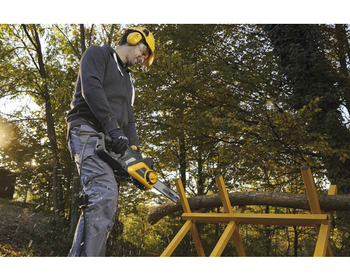 Muž reže drevo elektrickou pílou na kozlíku na záhrade.