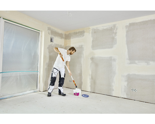 Muž renovuje izbu pomocou maliarskeho valčeka a vedra s farbou. Steny sú pripravené na maľovanie.