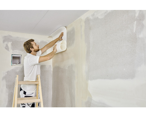 Muž tapetuje stenu s rolou tapety na rebríku
