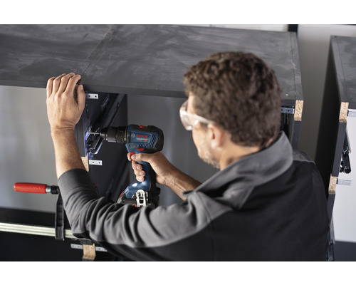 Remeselník pracuje s akumulátorovým skrutkovačom na kuse nábytku