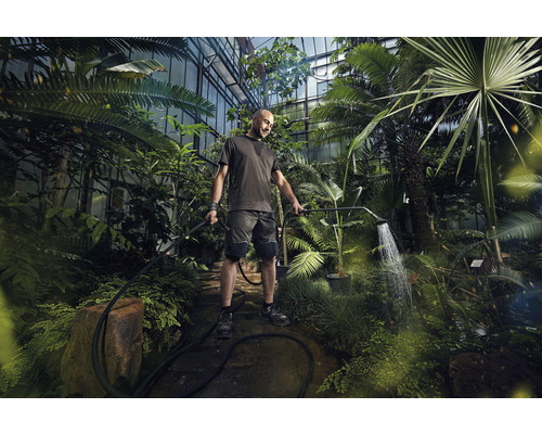 Muž zavlažuje rastliny v skleníku záhradnou sprchou.