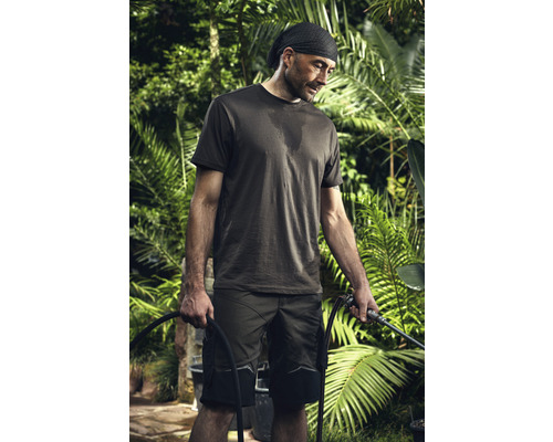 Muž v pracovnom odeve drží záhradnú hadicu v záhrade.