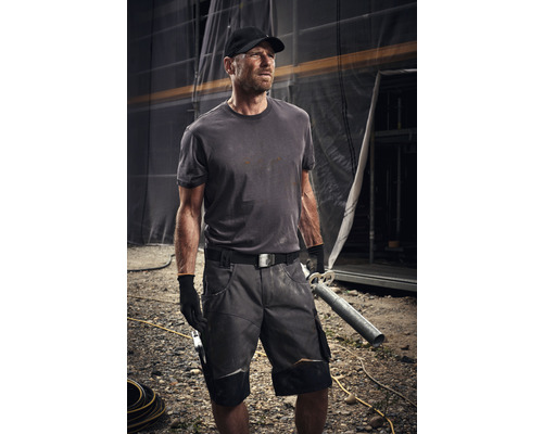 Remeselník nosí pracovný odev s kraťasmi, tričkom, opaskom a rukavicami na stavenisku