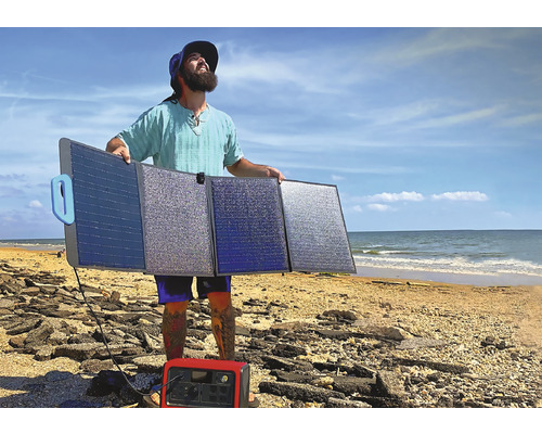 Muž drží solárny panel na pláži s prenosnou napájacou stanicou