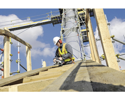 Stavebný robotník reže drevenú dosku kotúčovou pílou na lešení.