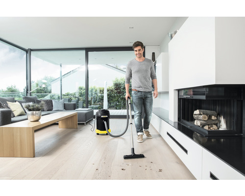 Muž vysáva drevenú podlahu viacúčelovým vysávačom vo svetlej obývačke