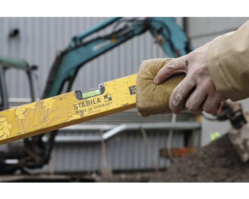 Vodováha sa čistí špongiou. V pozadí je bager.