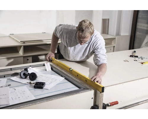 Remeselník kontroluje obrobok vodováhou na pracovnom stole.