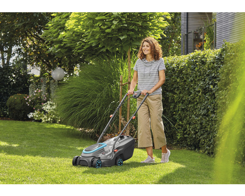 Žena obsluhuje kosačku na trávu v záhrade.