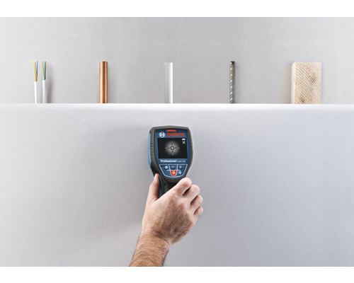 Ruka drží detektor Bosch na kontrolu stien, na detekciu elektrických vedení, medených rúr, plastových rúr, ocele a dreva