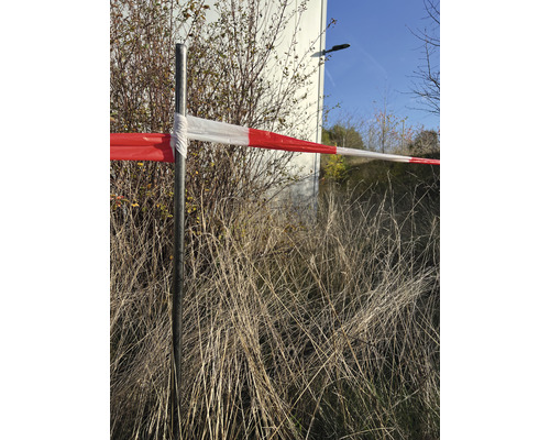 Výstražná páska na kovovom stĺpiku pred kríkmi a trávou