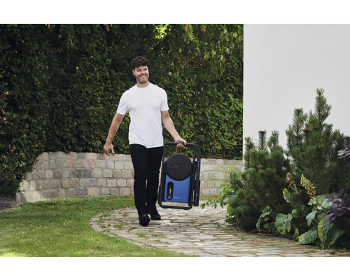 Muž nesie prenosnú tlakovú umývačku v záhrade.