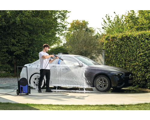 Muž umýva auto vysokotlakovým čističom v záhrade.