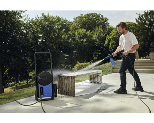 Muž čistí záhradnú lavicu vonku pomocou vysokotlakového čističa.