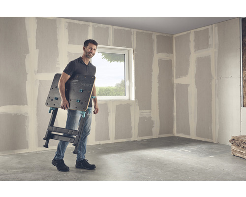 Muž nesie pracovný stôl Wolfcraft Master 650 v miestnosti so sadrokartónovými stenami