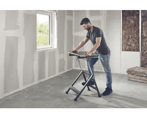 Muž pracuje s pracovným stolom v miestnosti so sadrokartónovými stenami a oknom.