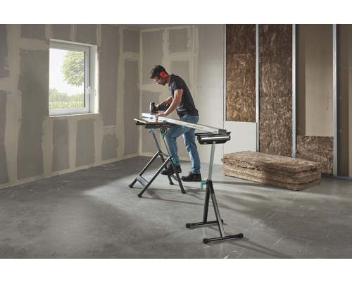 Muž pracuje s priamočiarou pílou na obrobku na ponku Wolfcraft v miestnosti so sadrokartónovými doskami a izolačným materiálom.