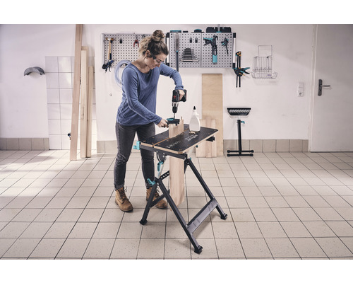 Žena pracuje s vŕtačkou na pracovnom stole v dielni.