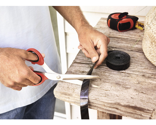 Osoba strihá čiernu plastovú pásku nožnicami na drevenom stole.