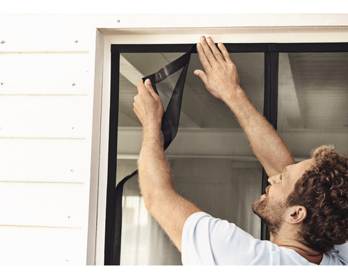 Muž inštaluje do okna sieť proti hmyzu