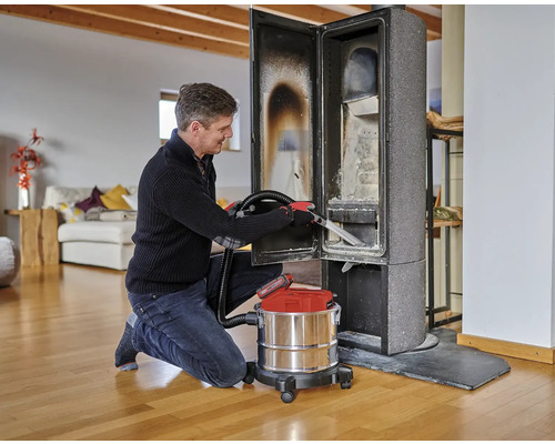 Muž čistí kachle na drevo pomocou vysávača popola v obývacej izbe.