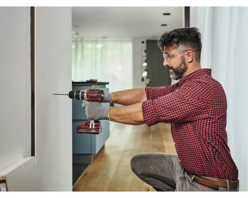 Muž vŕta otvor do steny pomocou akumulátorového vŕtacieho skrutkovača.