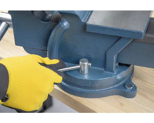 Zverák na pracovnom stole ovládaný rukou v pracovnej rukavici.