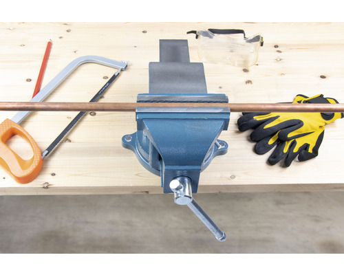 Pracovný stôl so zverákom, medená rúrka, ručná píla, ochranné okuliare a pracovné rukavice