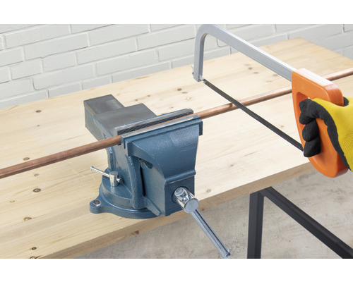 Zverák drží medenú rúrku, ktorá sa reže pílkou na kov.