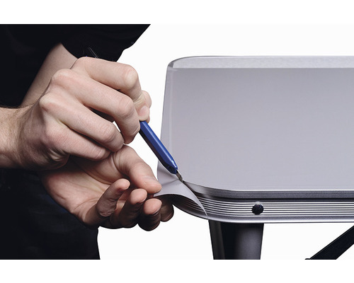 Osoba orezáva fóliu na povrchu nožom.