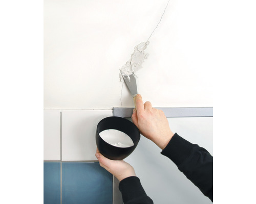 Osoba špachtľou vypĺňa trhlinu v stene. Drží sa miska s výplňovým materiálom.
