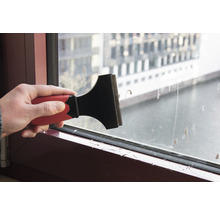 Ruka používa škrabku na sklo na čistenie okna.