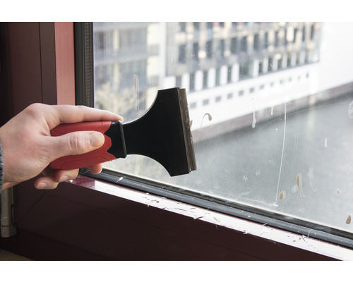 Ruka používa škrabku na sklo na čistenie okna.