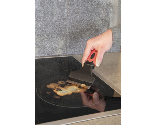 Osoba čistí varnú dosku pomocou škrabky na sklo.