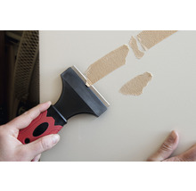 Muž odstraňuje staré zvyšky lepiacej pásky zo steny škrabkou.