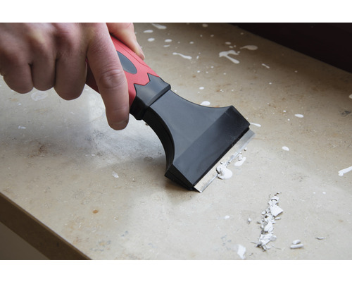 Remeselník používa škrabku na odstránenie zvyškov farby z povrchu.