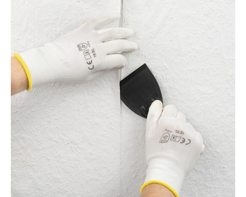 Osoba vyhladzuje tapetu špachtľou a ochrannými rukavicami