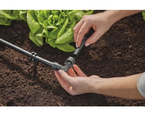 Záhradná scéna so zavlažovacím systémom a osobou pripevňujúcou spojovací kus.