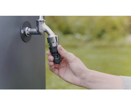 Ruka pripevňuje hadicovú spojku na vodovodný kohútik na zavlažovanie záhrady.