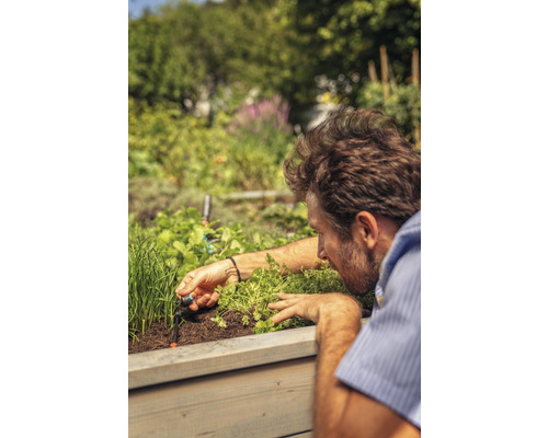 Muž inštaluje zavlažovací systém do vyvýšeného záhona s bylinkami a rastlinami.