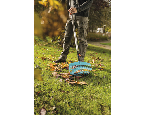 Osoba hrable lístie hrabľami na trávniku.