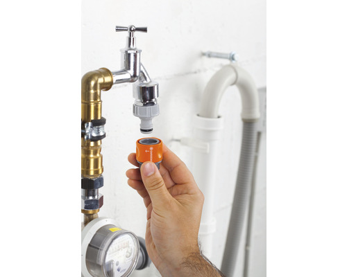 Ruka pripevňuje adaptér Gardena k vodovodnému kohútiku na zavlažovanie záhrady