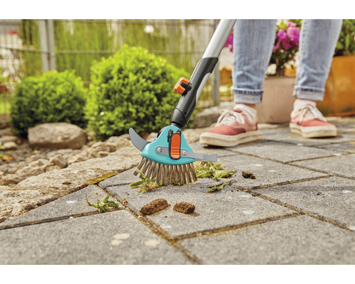 Kefa na škáry s teleskopickou rukoväťou používaná na odstraňovanie buriny z dlažobných kociek