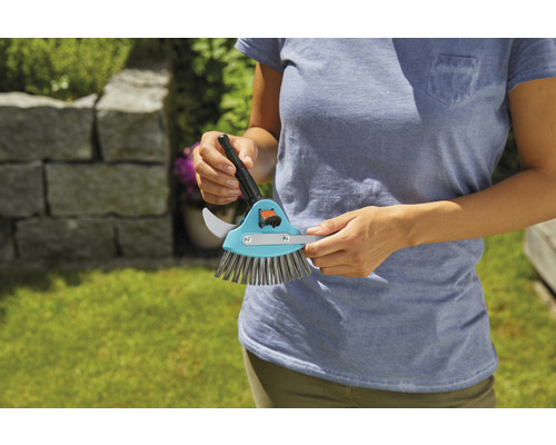 Osoba drží kefu na škáry so škrabkou na škáry a kefou.