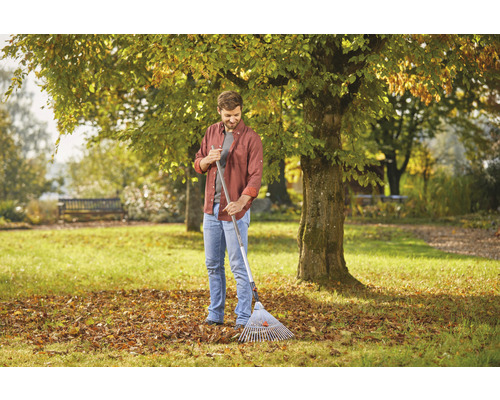 Muž hrabe lístie hrabľami na lístie v záhrade.